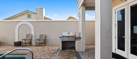 Zona de piscina con una parrilla, sillas y una puerta.
