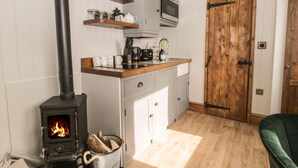 Una cocina con estufa de leña, armarios blancos y puerta de madera.