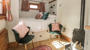 Un dormitorio acogedor con cama, una silla, una mesita, una ventana con cortinas, una chimenea y techo de madera.
