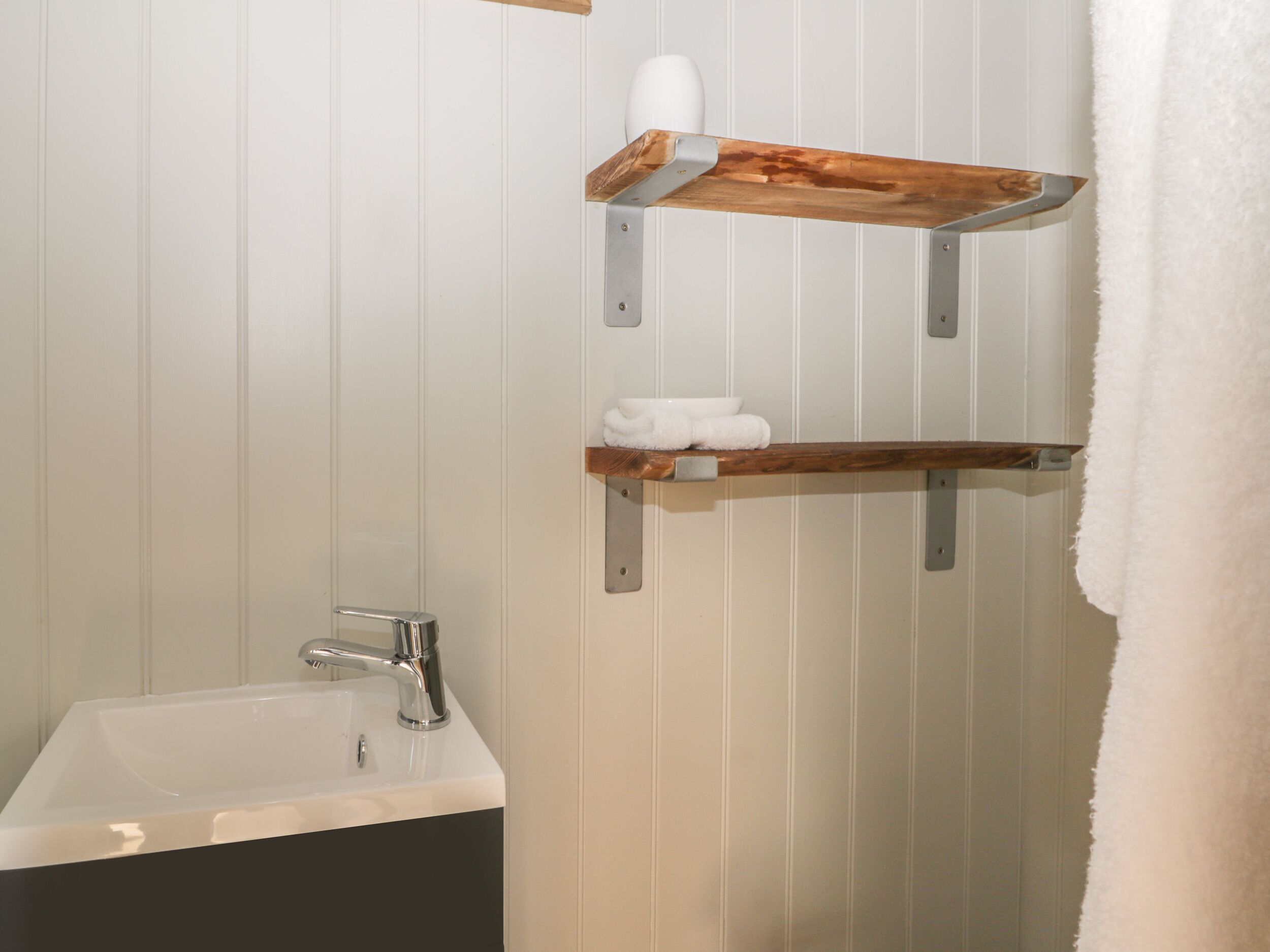 A bathroom with a white sink, a mirror, and wooden shelves holding towels.
