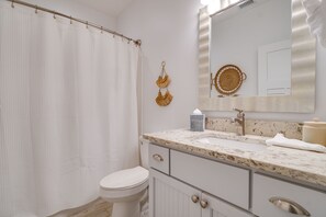 A bathroom with a white toilet, a shower curtain, a sink with a marble countertop, a mirror, and a towel. - Beach House - The Starfish By Panhandle Getaways (Panama City Beach)
