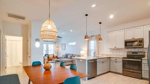 A modern kitchen with white cabinets, stainless steel appliances, and a wooden dining table. - Beach House - The Starfish By Panhandle Getaways (Panama City Beach)