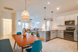 A modern kitchen with white cabinets, stainless steel appliances, and a wooden dining table. - Beach House - The Starfish By Panhandle Getaways (Panama City Beach)