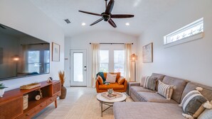 A spacious living room with a ceiling fan, a large flat-screen TV, a wooden console table, a beige sofa, and a patterned rug. - Beach House - The Starfish By Panhandle Getaways (Panama City Beach)