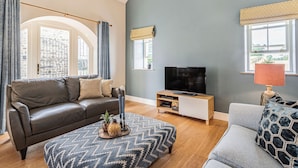 Ein Wohnzimmer mit Sofa, Ottoman, TV-Schrank und einem Fenster mit Blick.