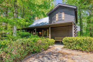 A rustic cabin with a porch, surrounded by dense greenery.