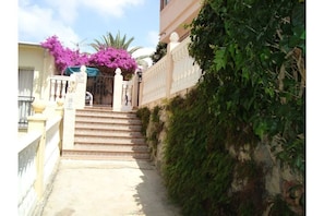 Stroll through the beautifully landscaped entrance, flanked by lush greenery and a traditional gate.