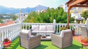 En balkon med hvid sofa, fletstole og plantekasser.