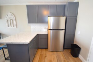A kitchen with grey cabinets, a stainless steel refrigerator, and a white tiled backsplash.