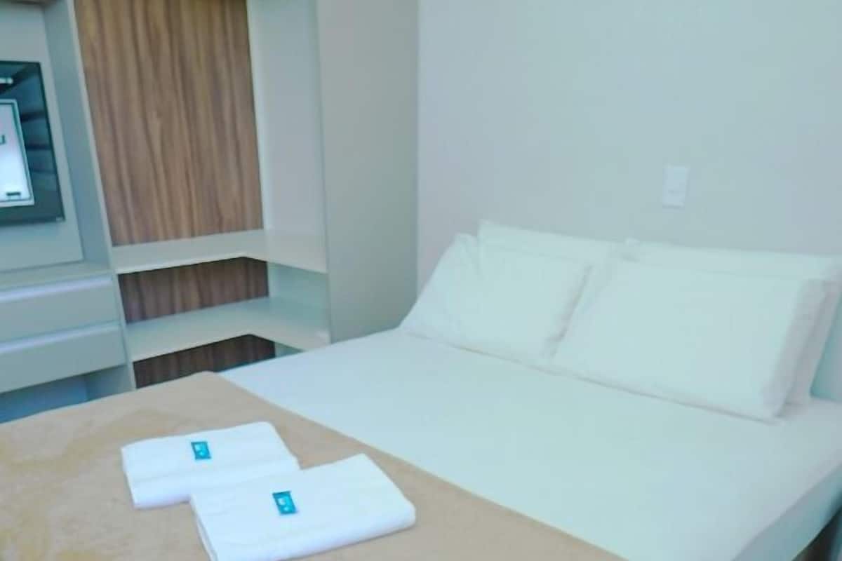 Una habitación de hotel con cama, un armario de madera y una pequeña mesa con mantel blanco.