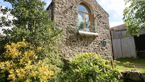 A stone building with a small arched window and a weather vane on top. - Ty Gwennol (Beaumaris)