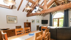 A dining area with a wooden table and chairs, a television on the wall, and a window with curtains. - Ty Gwennol (Beaumaris)