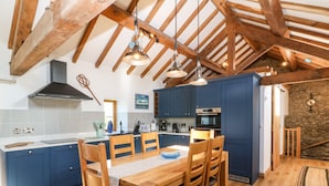 A kitchen with wooden beams, a dining table with chairs, and a stone wall. - Ty Gwennol (Beaumaris)