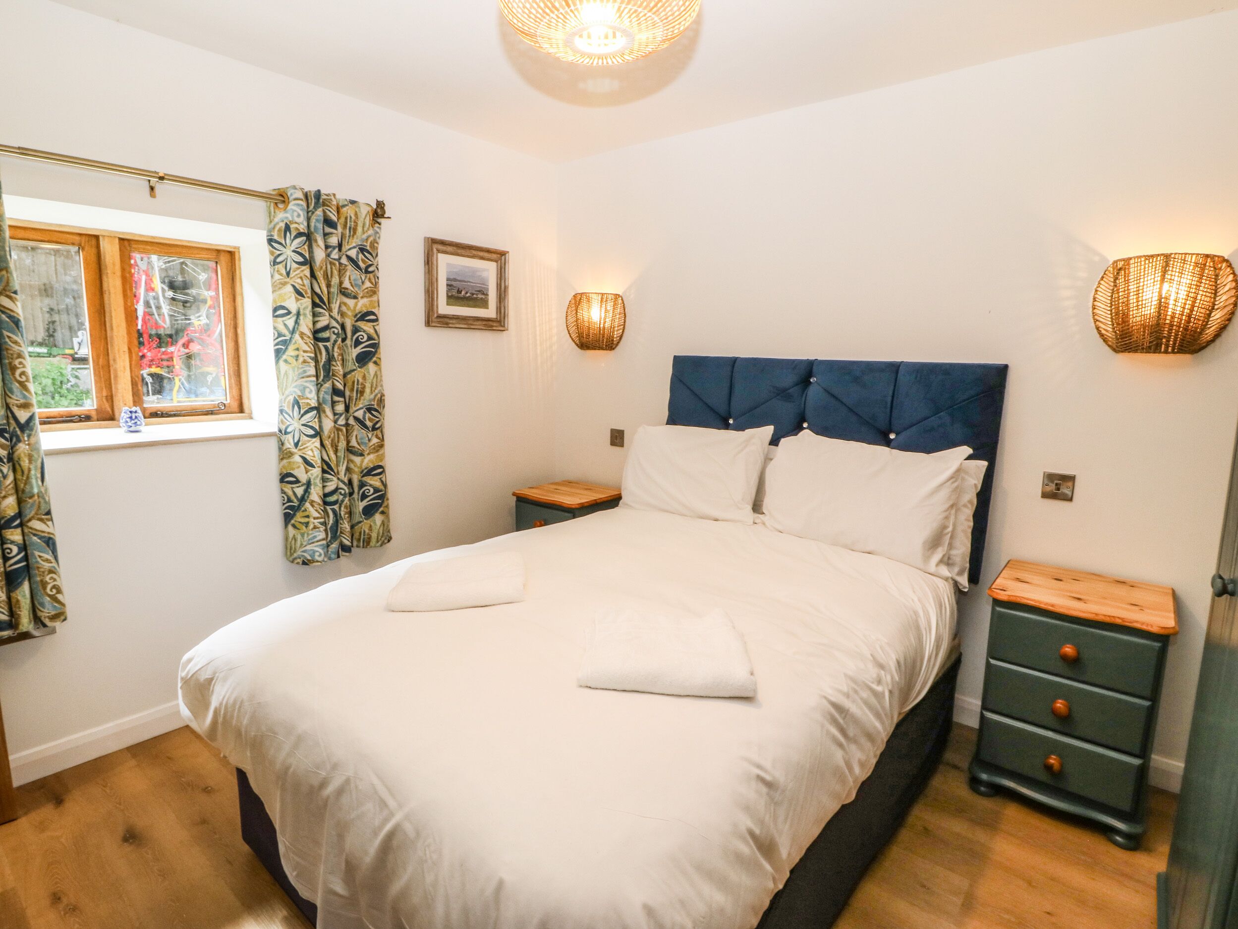 A bedroom with a large bed, two bedside tables, a window with curtains, and wall-mounted lamps.