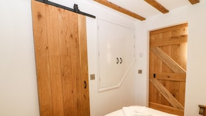 A bedroom with a wooden wardrobe, a white door, and a wooden wall panel. - Ty Gwennol (Beaumaris)