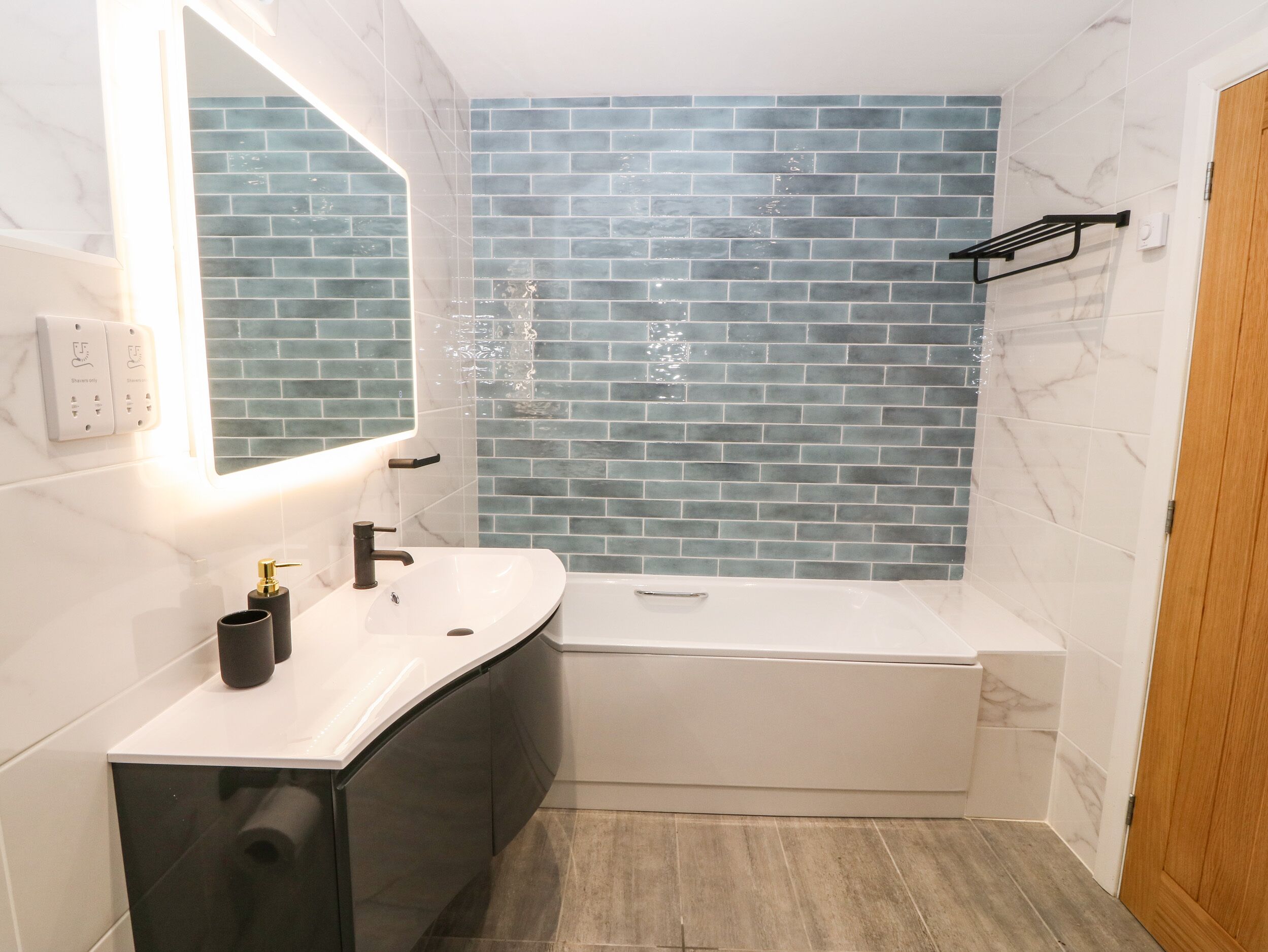 A modern bathroom with a white vanity, a large mirror, and a blue-tiled shower wall.