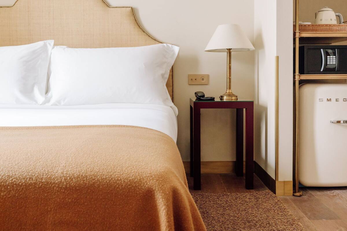 Una camera d'albergo con un letto, un comodino, una lampada, un forno a microonde e un piccolo armadietto.