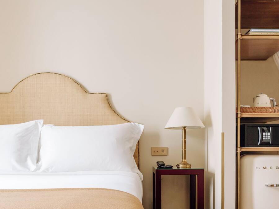 Una habitación de hotel con una cama, una mesita de noche, una lámpara, un microondas y un pequeño armario.