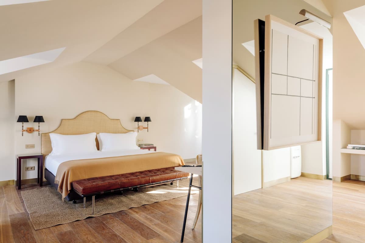 Una camera da letto con un letto, lampade sui comodini, una panca, un tappeto e pavimento in legno.