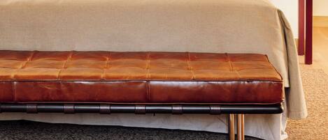 A neatly made bed with a green pillow, a wooden bench, and two wall-mounted lamps.