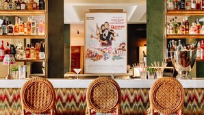 Un coin bar avec des fauteuils en osier, des étagères remplies de bouteilles d’alcool et une affiche de James Bond 007.