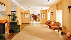 Un hall d’entrée spacieux avec un plancher en bois, des fauteuils verts, une cheminée et un grand arrangement floral au centre.