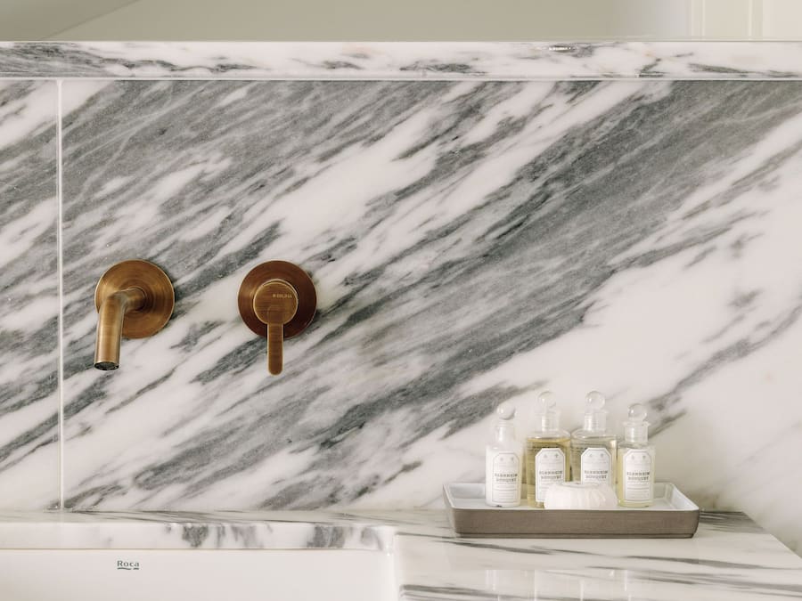 A bathroom with a marble sink, gold fixtures, and a tray with toiletries.