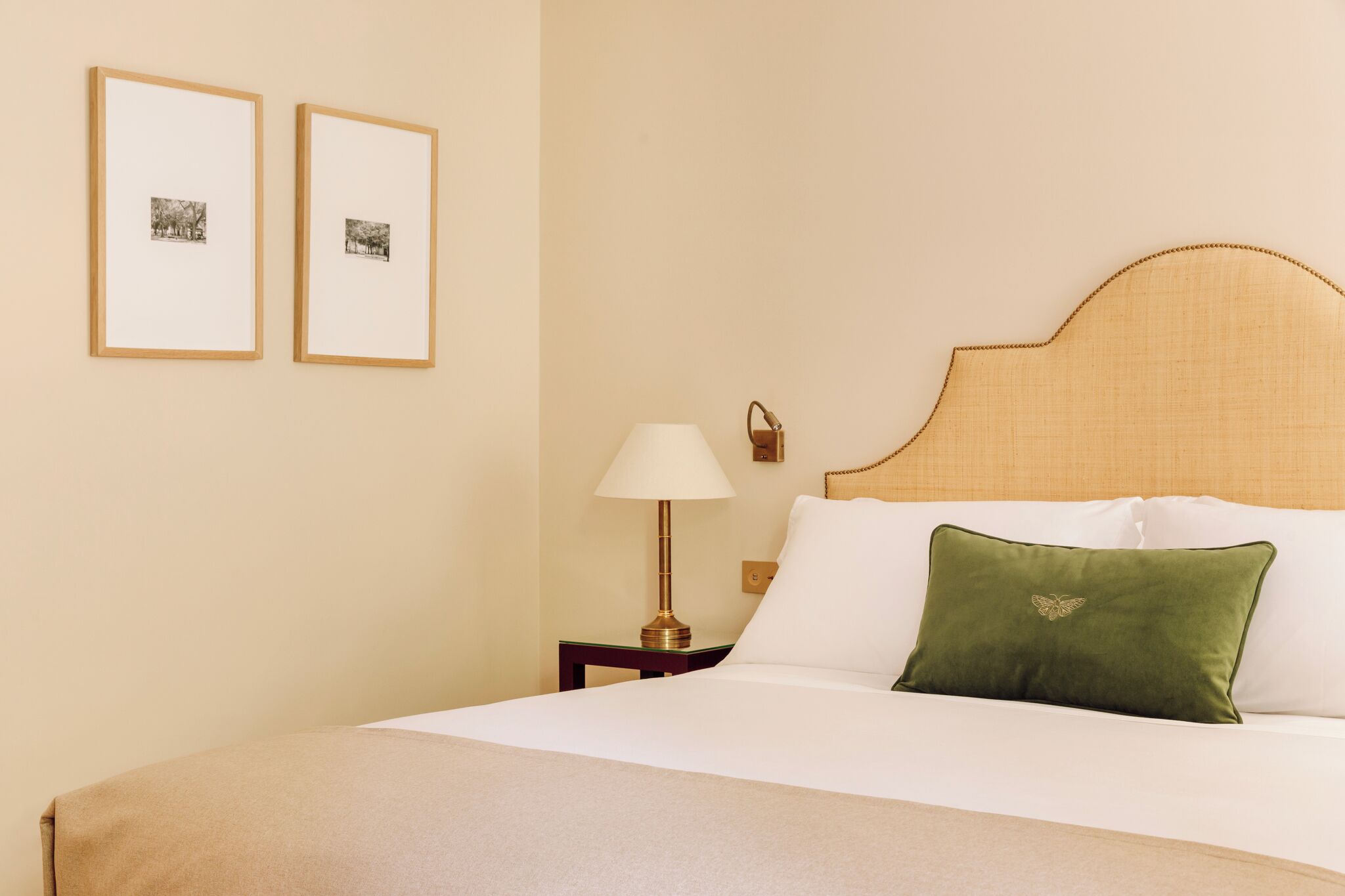 Un lit bien fait, avec un oreiller vert, une lampe de chevet et deux tableaux encadrés accrochés au mur.