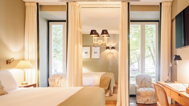 Une chambre d’hôtel avec un grand lit, deux fauteuils, un bureau et un lustre.