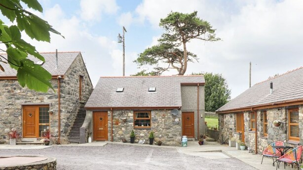 Un bâtiment en pierre avec une allée de gravier, des portes en bois et un arbre en arrière-plan.