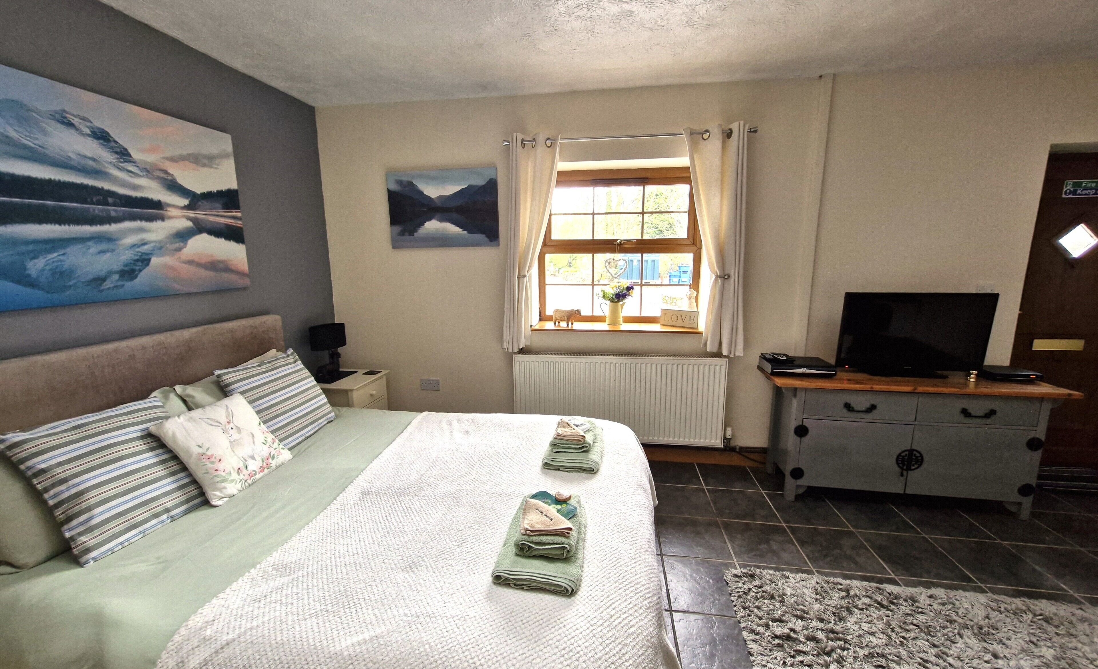 A bedroom with a bed, a TV, a dresser, a window with curtains, and a painting on the wall.