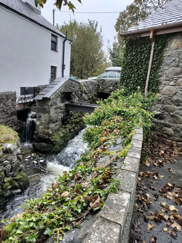 A stone bridge over a small stream with a waterfall, surrounded by greenery and a stone wall. - Barn conversion at the old Watermill - Snowdonia & Zip Line close by. (Pentir)