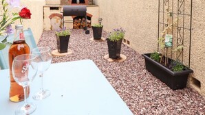 Une terrasse extérieure avec un mur en pierre, un four en briques, un barbecue et des plantes en pot.