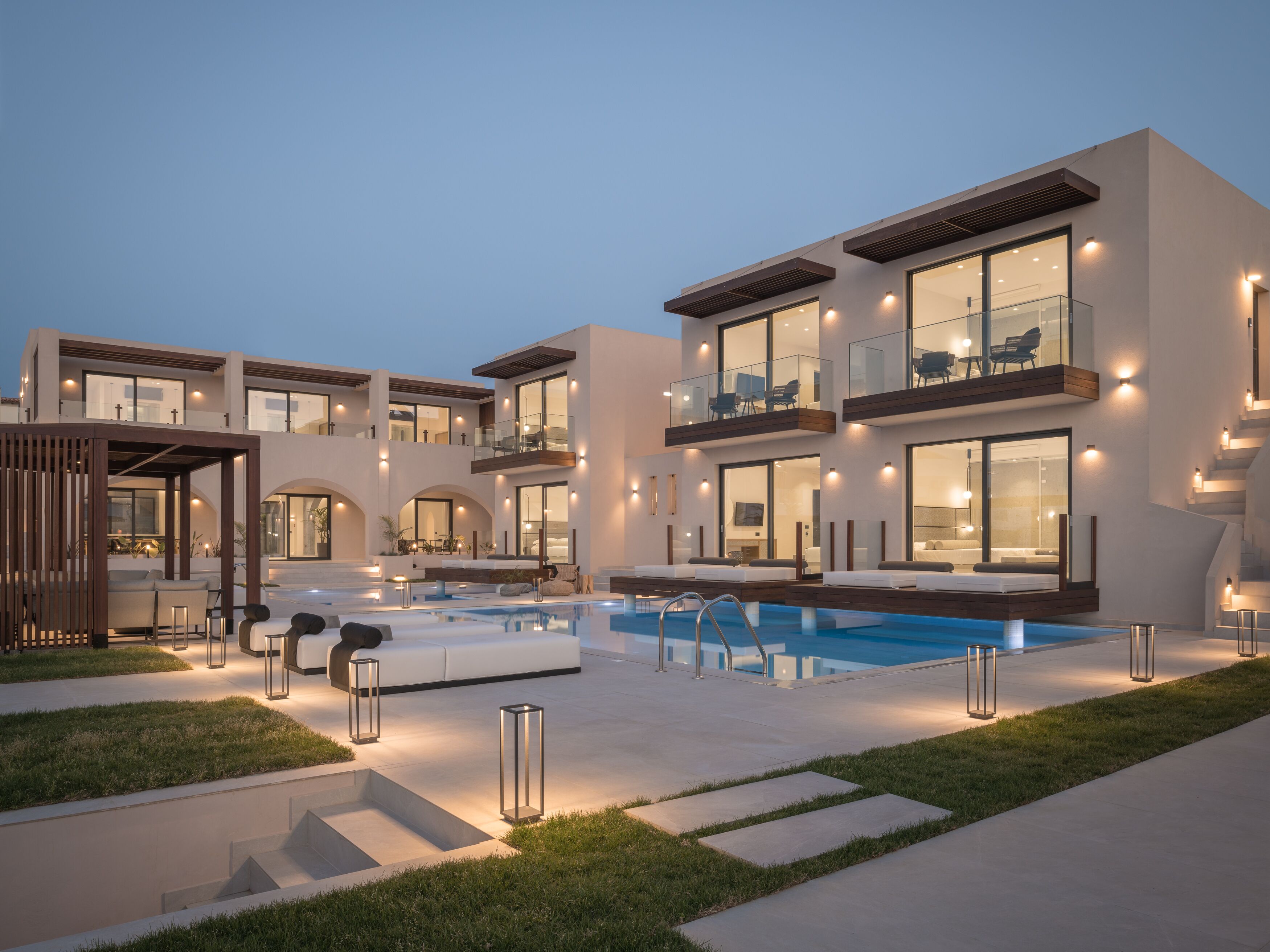 Un moderno edificio residencial de varios pisos con piscina, mobiliario exterior y una zona de balcón bien iluminada.