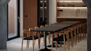 Ein moderner Konferenzraum mit langem Tisch und Stühlen, einer Küchenzeile mit Fliesenrückwand und einem großen, rundbogigen Durchgang.