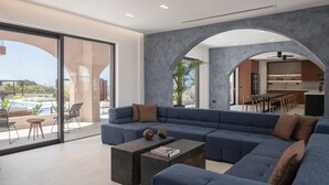 Ein modernes Wohnzimmer mit einer Eckcouch, einem Couchtisch und einem Essbereich, im Hintergrund ist eine Küche zu sehen.