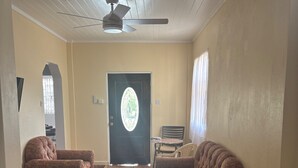 Una sala de estar con sofás estampados, piso de madera, ventilador de techo y una puerta con vidriera.