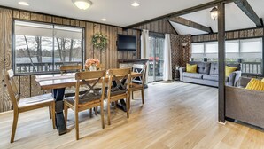 A spacious room with a wooden dining table, chairs, a sofa, and a television. - Pocono Lake Home w/ Fire Pit: Walk to Ski Hill! (Pocono Lake)