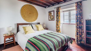 Un dormitorio con techo de madera, una cama con manta de rayas coloridas, un tapiz de pared tejido y una ventana con cortinas.