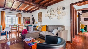 Un salón acogedor con techo de madera, un sofá gris, un sillón negro y una zona de comedor con sillas y mesa de madera.