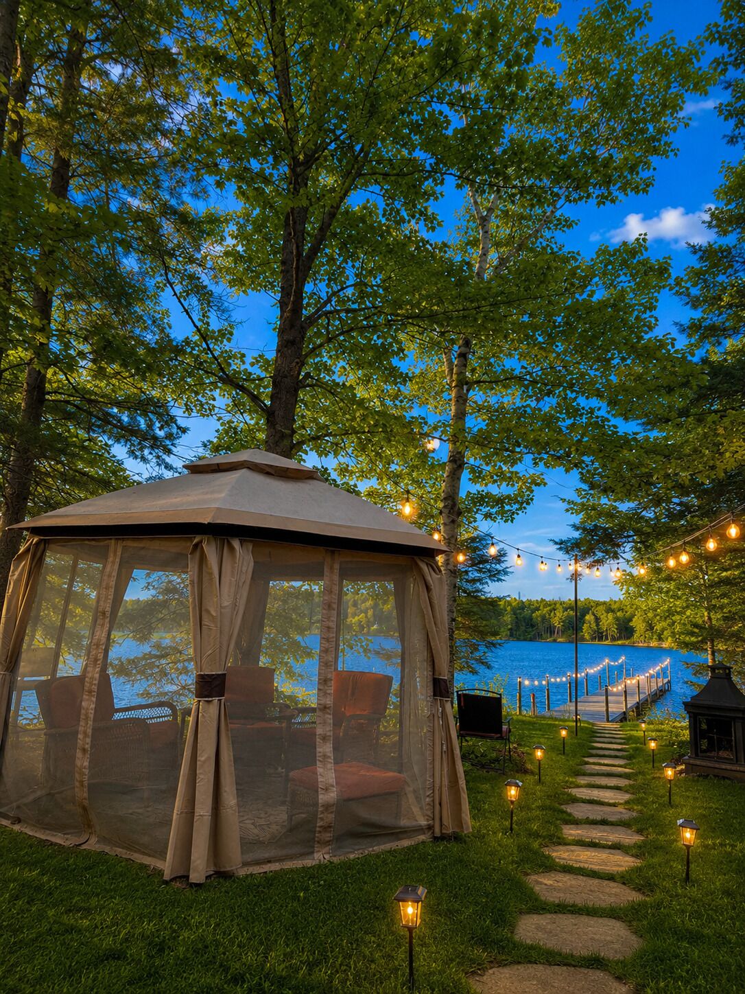A gazebo with a covered seating area, surrounded by trees and a pathway leading to a dock.
