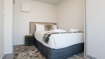 A bedroom with a bed, a bedside table, a small stool, and a checkered floor.