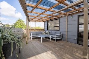 A covered patio with a wooden deck, a grey sofa, and a table.
