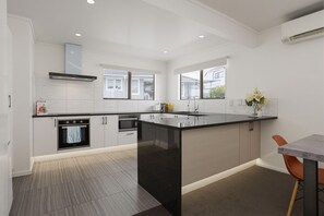 A modern kitchen with a central island, built-in oven, and a large window providing natural light.
