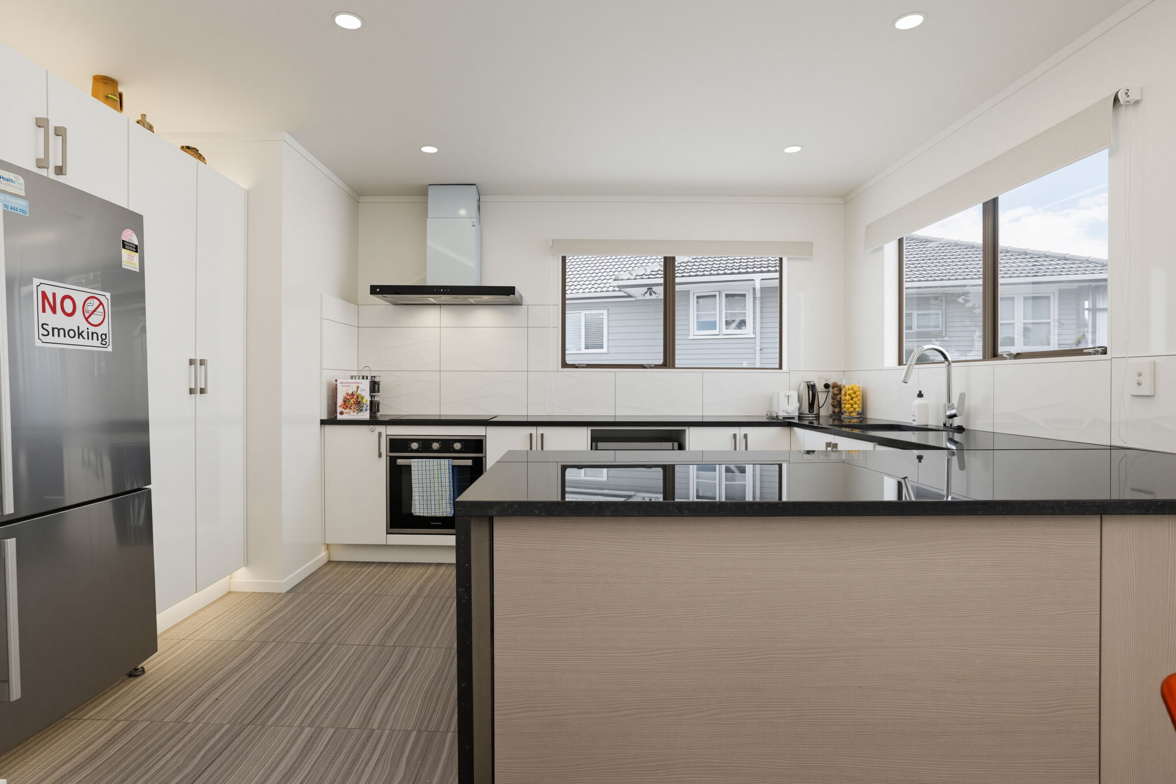 A modern kitchen with a stainless steel refrigerator, a no-smoking sign, a built-in oven, and a large window.
