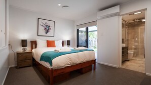 Um quarto moderno com uma cama de madeira, uma mesa de cabeceira, um abajur, uma obra de arte emoldurada e vista para o banheiro.
