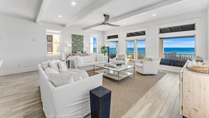 A spacious living room with white furniture, large windows, and a view of the ocean. - Wilder Dreams - Gulf Front, Pool, Gated Community, Steps to Rosemary Beach (Seacrest)