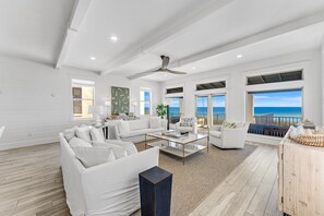 Ein großzügiges Wohnzimmer mit weißen Möbeln, großen Fenstern und Meerblick.