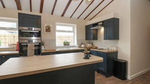 Une cuisine moderne dotée d’un îlot central, de meubles de rangement aux couleurs sombres, d’un four encastré et de luminaires suspendus.
