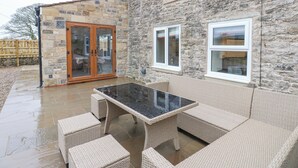 Un bâtiment en pierre avec une porte en verre, une terrasse dotée de meubles en osier et un sol carrelé.